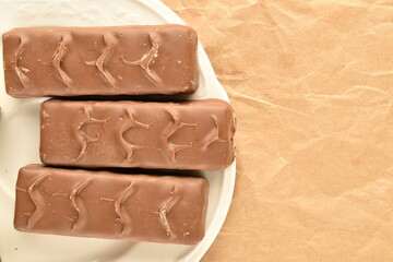 Three chocolate bars on a white plate, close-up, on brown paper.
