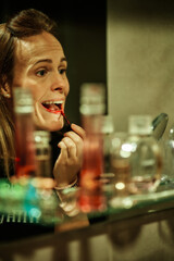 young woman painting her lips in front of the mirror facing the front