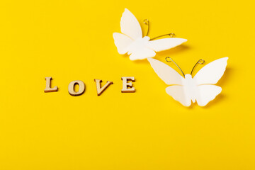 Pair of plastic butterflies and text Love on yellow background. Concept of romance. Copy space left.