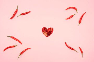 A red heart and red hot chili peppers around it lie on a pink background