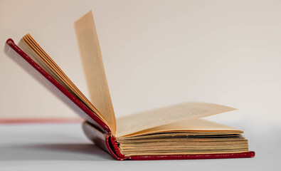 Close up of an open antique book with red leather covers and pages standing on white background