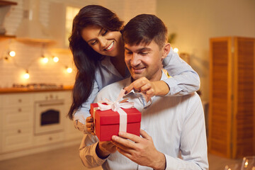 Smiling loving young couple hugging and unpacking holiday present during Valentines day celebration at home together. Love, Valentines day, togetherness, birthday, anniversary, dating concept