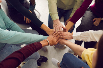 Mixed race people sitting in circle and putting hands together in business team meeting or group therapy session. Community, trust, success, motivation, mutual responsibility, unity, support concepts - obrazy, fototapety, plakaty