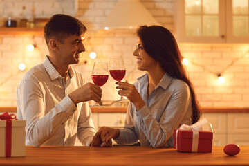 Smiling loving couple sitting with glasses of wine, holding hands and looking at each other during Valentines day celebration at home together. Love, Valentines day, togetherness, dating concept