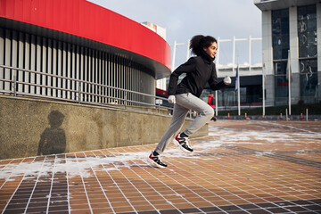 Fototapeta na wymiar Female athlete sprinting forward on a city square