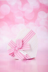 Gift in the form of a heart on a pink background with bokeh