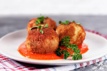 Delicious hot italian arancini - rice balls stuffed with cheese in tomato sauce, in a plate on an old wooden table