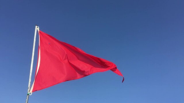 Un drapeau rouge flotte au vent au bord d&rsquo;une plage pour indiquer que la mer est dangereuse et que la baignade est interdite.