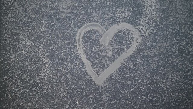 A heart drawn on a frozen winter window at sunset.