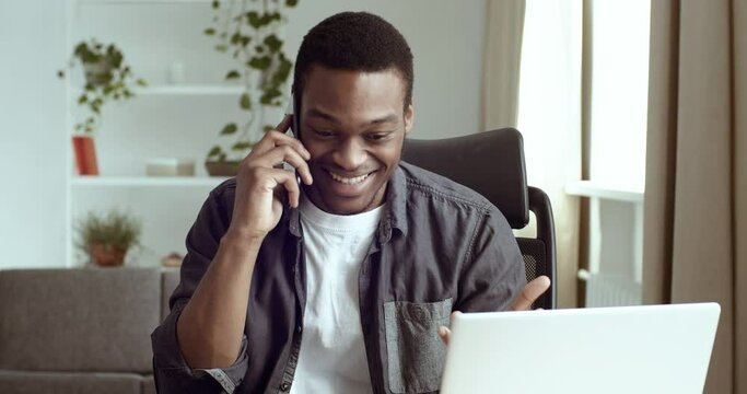 Portrait of happy african american business man salesman student talking on smart phone wins gets to know good news gets opportunity new job says yes feels delight sitting at table in office or home