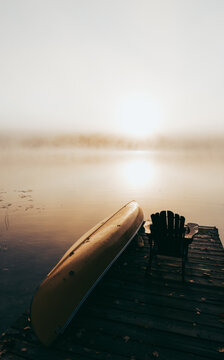 Empty dock with overturned canoe on a foggy morning on a calm lake.