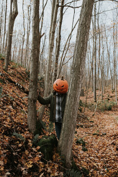 Man wearing scary carved pumpkin head in the woods for Halloween.