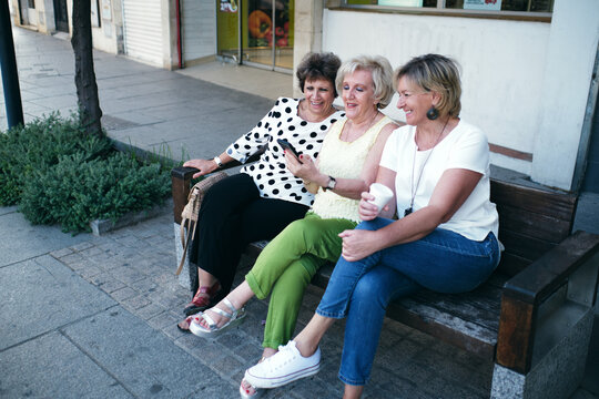 women happily sitting on a bench smiling and showing off their cell ph