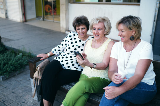 Mature women smiling at the mobile phone sitting on a bench