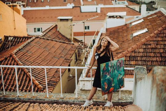 Female artist holding canvas while standing on tiled roof with view