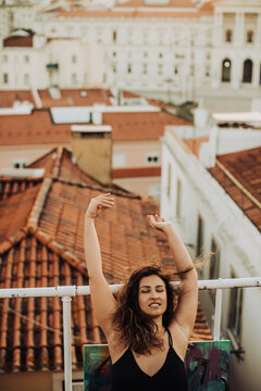 Woman sitting on tiled roof with hands up, enjoying face expression