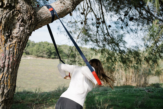 TRX sport team. Young woman doing exercises outdoors in a park. Strap
