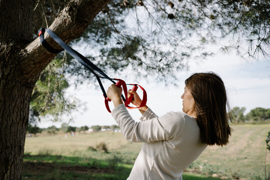 TRX sport team. Young woman doing exercises outdoors in a park. Strap