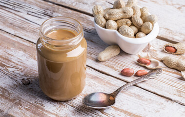 Peanut butter in a glass jar on a wooden background. Delicious and healthy breakfast.