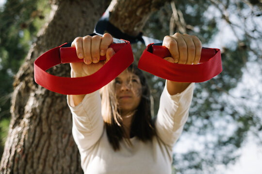 TRX sport team. Young woman doing exercises outdoors in a park. Strap
