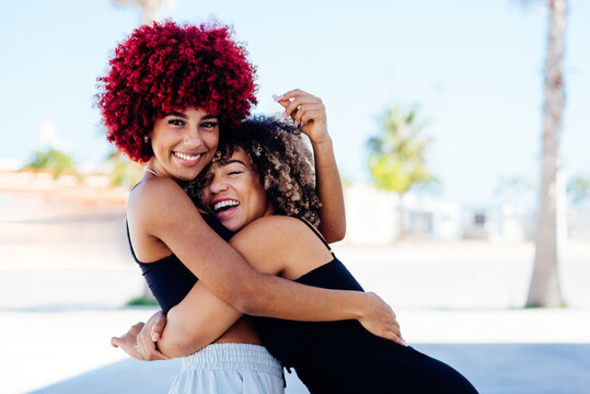 Two attractive latin girls with afro hair hugging each other amicably.