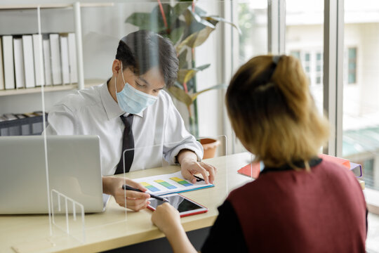 Business Man Workers Wearing Face Mask And Clear Shield Having Discussion Through Glass Partition At The Office