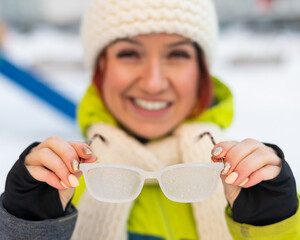 Smiling caucasian woman takes off frozen glasses outdoors in winter. The girl is cold.