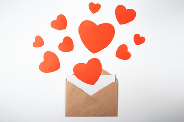 Craft envelope with a blank sheet and red paper hearts on the light (white) background. Flat lay, top view. Romantic love letter for Valentine's day concept.