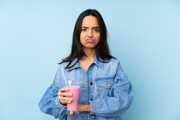 Young woman with strawberry milkshake over isolated blue background feeling upset