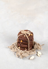Vegan dessert chocolate cookies with whole peanuts, tied with jute thread on a linen napkin on a light background in rustic style copy space
