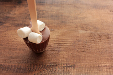 Hot chocolate with marshmallow on a stick. Hot chocolate stirrer on wooden background. 