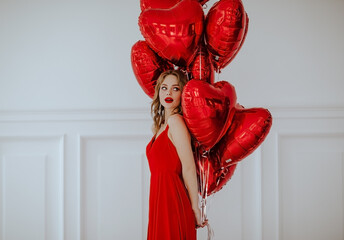 Pretty blond woman in red evening dress and red lips posing with bunch of red balloons against white background. Copy space.
