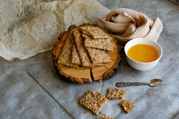 Healthy and nutritious diet bread with sesame and sunflower seeds on a thin crunchy malt base. Near natural bee honey and a wooden stand sawn