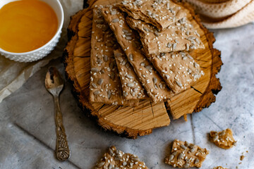 Healthy and nutritious diet bread with sesame and sunflower seeds on a thin crunchy malt base. Near natural bee honey and a wooden stand sawn