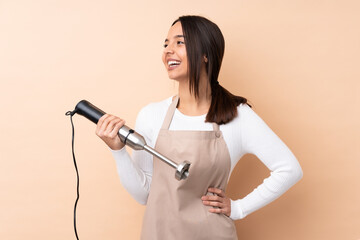 Young brunette girl using hand blender over isolated background happy and smiling