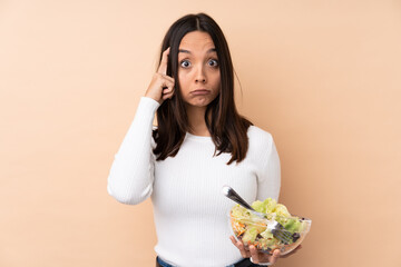 Young brunette girl holding a salad over isolated background thinking an idea