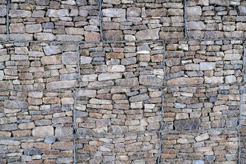 Metal Cage filled with rocks texture . Stone wall with metal grid as background.  Gabion net