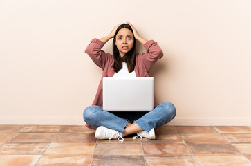 Young mixed race woman with a laptop sitting on the floor doing nervous gesture
