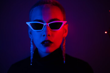 Portrait of a young woman with a short male haircut in sunglasses in neon light in the studio