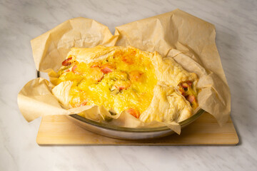 Pie with tomatoes and sausage from puff pastry in parchment paper in glass form on the table