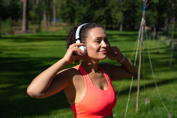 Smiling woman in sportswear standing in the park and touching headphones on her head