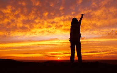 Fototapeta premium Woman hiker with hands up arms during sunset. Silhouette of an unrecognizable girl.
