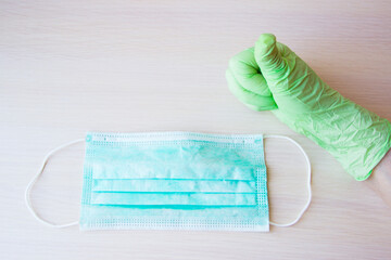 A woman's hand in green medical gloves and medical mask on a light wooden background. Supplies for quarantine isolation period. Hygiene, coronavirus, health concept. Medical supplies for doctors.