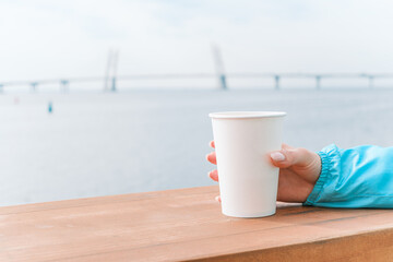 A glass of coffee on the background of the sea. Close-up of a female hand with a hot drink.