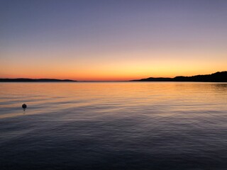 Purple and orange calm sunset above water with hills