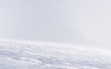 The mountain slope is completely covered with a layer of snow with traces of the wind on it.