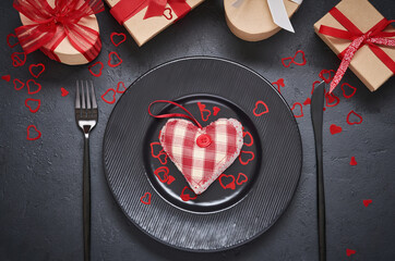 Valentine's day or romantic dinner. Empty black plate with heart made of fabric toys. Festive server on a dark background table with place for text. Top view.