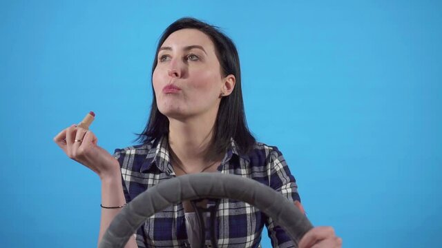 Young woman applies makeup while driving car on blue background of slow mo, isolated