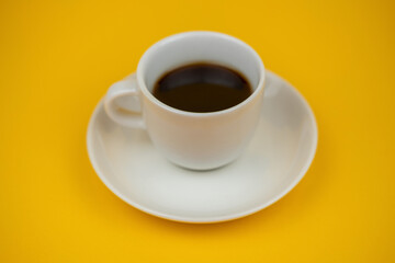 A white cup of coffee on a yellow background