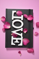 White wooden letters the word "love" on black notebook In the pink background
Valentine concept
